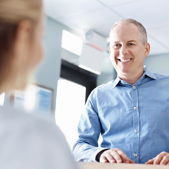 Smiling man checking in at dental office reception desk