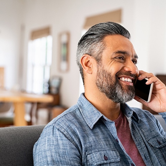 Man in blue shirt smiling while talking on cellphone 