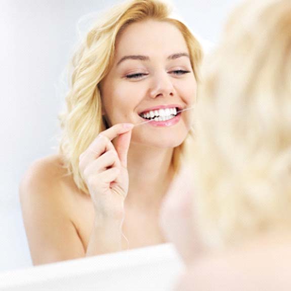 Woman using floss to prevent dental emergencies in Glastonbury