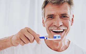 Smiling man with dental implants in Glastonbury brushing his teeth