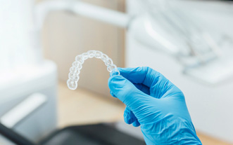 Dentist with blue glove holding clear aligner
