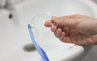 Patient using toothbrush to clean aligner