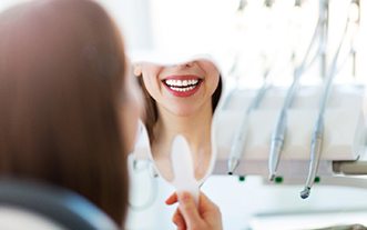 Woman checking smile in mirror at dentist’s office