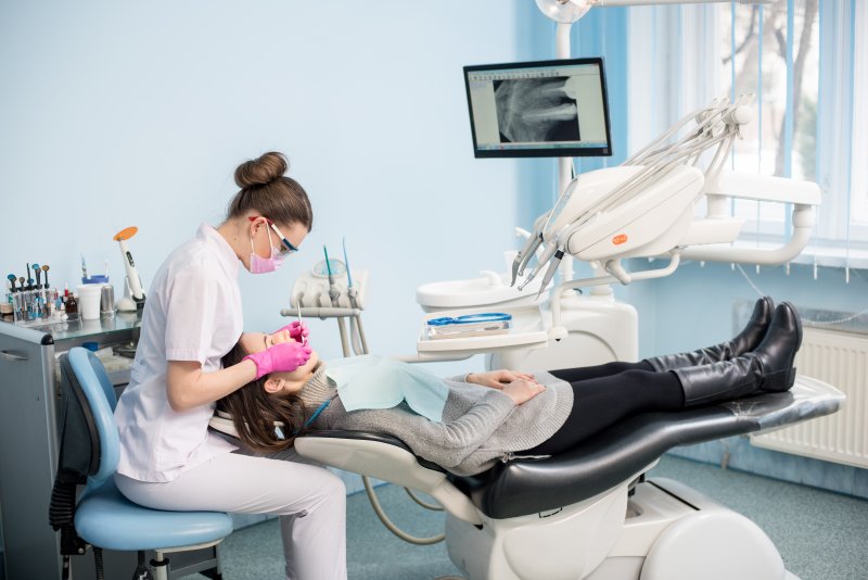 a dentist looking at a female patient’s mouth while the woman lies back in the dentist’s chair