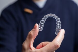 Dentist holding clear aligner in foreground. 