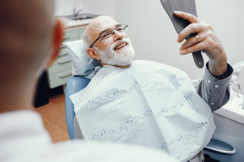 An older man admiring his new dentures with a hand mirror