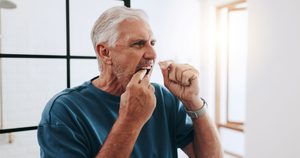 Man in blue shirt with white hair flossing his teeth